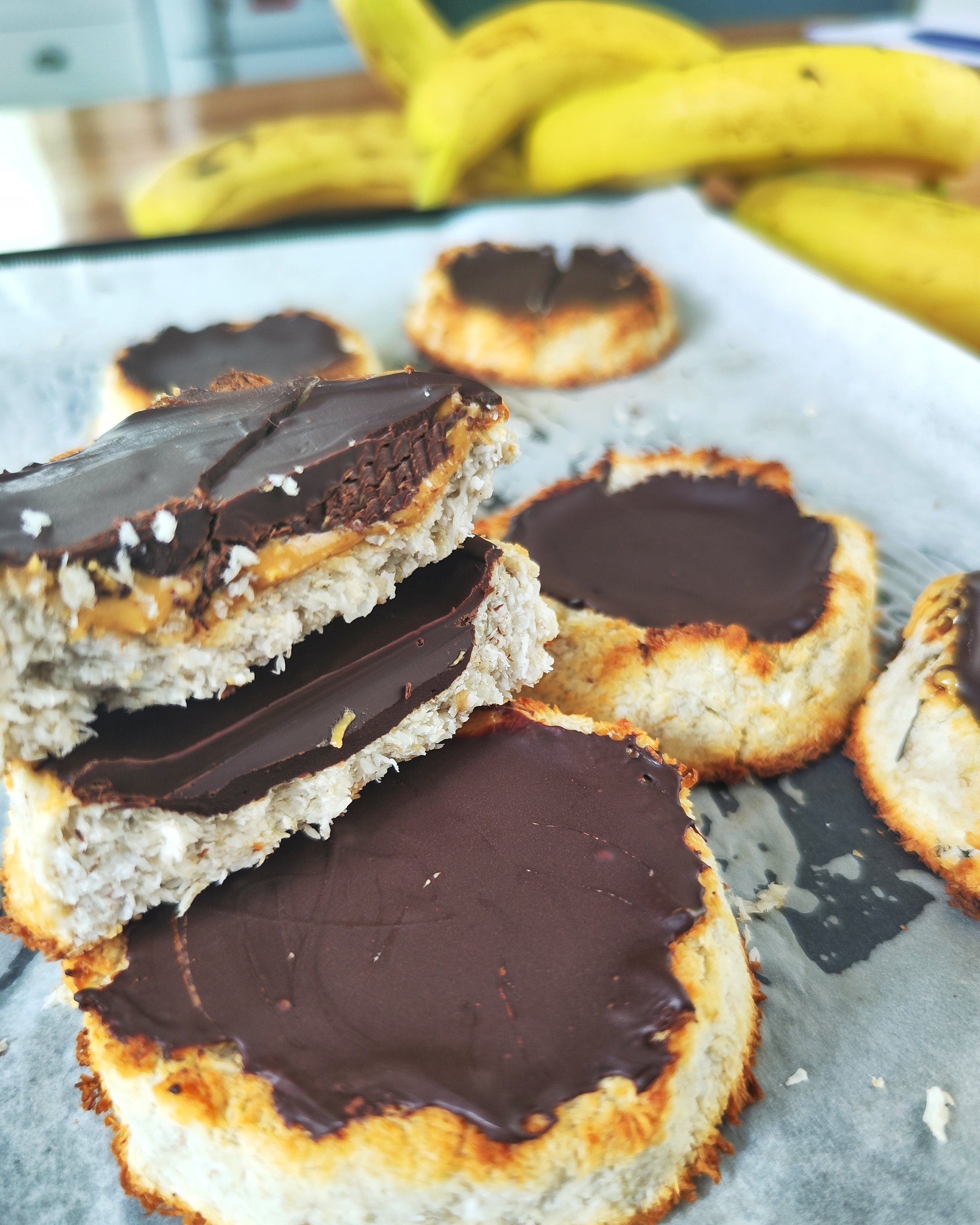 Three-ingredient banana coconut cookies topped with dark chocolate on a baking tray.