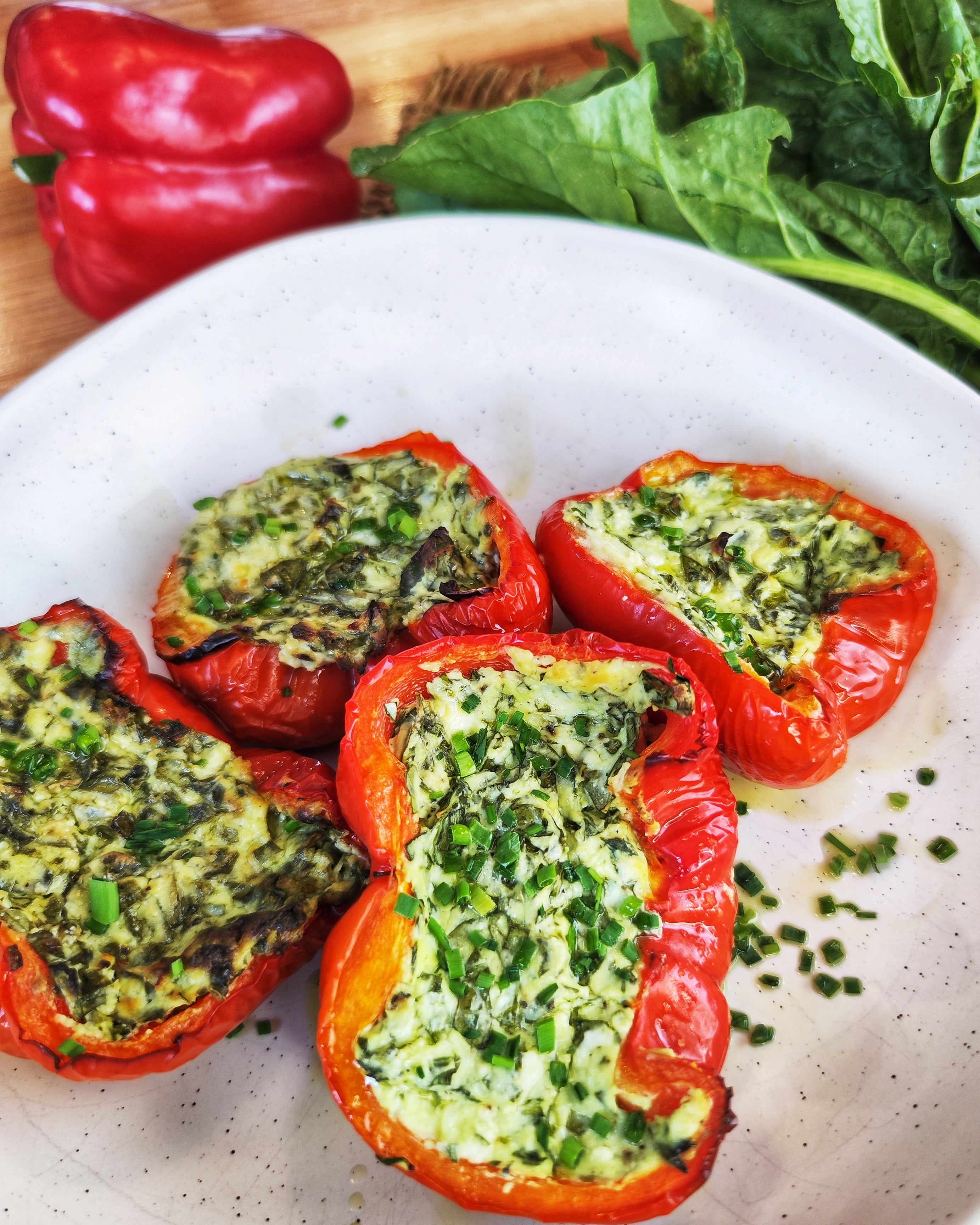 Baked capsicum halves filled with creamy feta and spinach mixture, topped with fresh herbs and lightly golden from the oven.